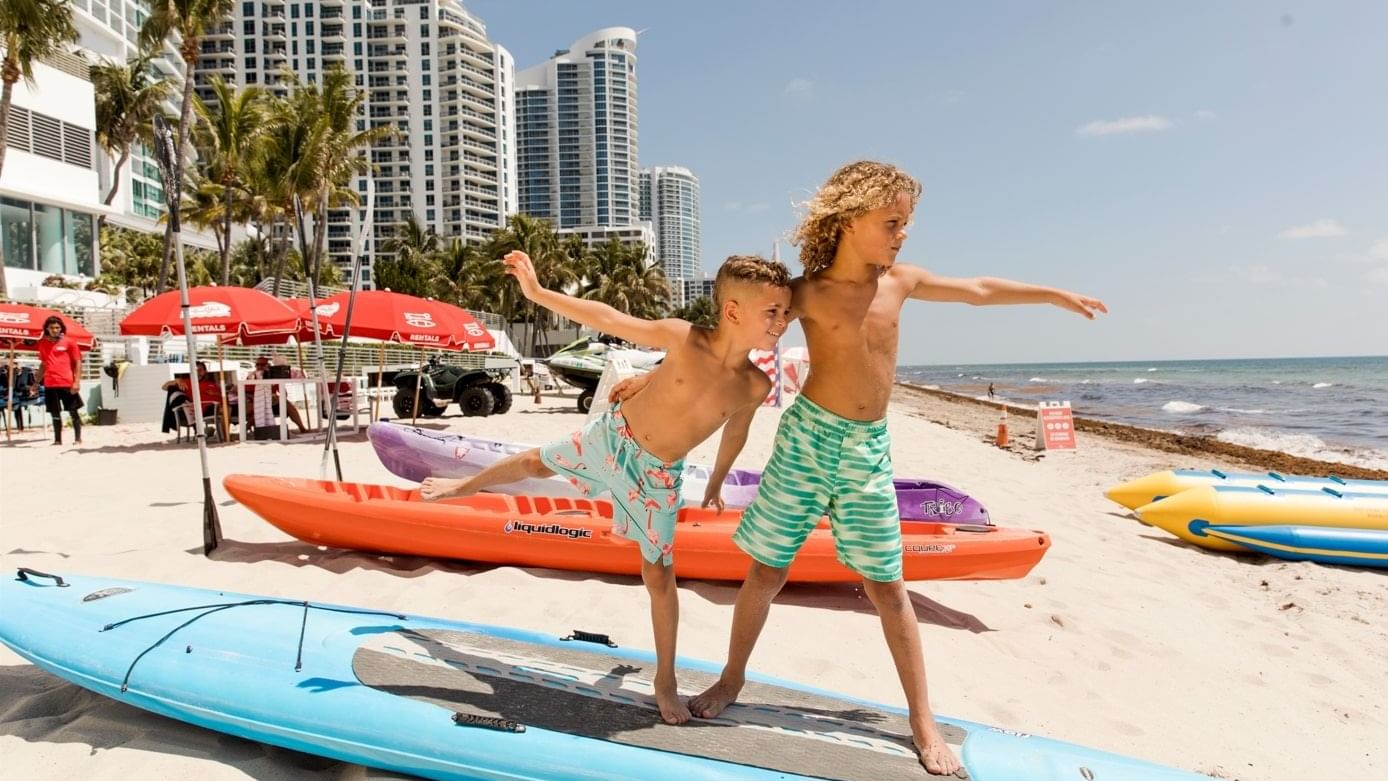 Two boys on kayaks at a sandy beach near The Diplomat Resort