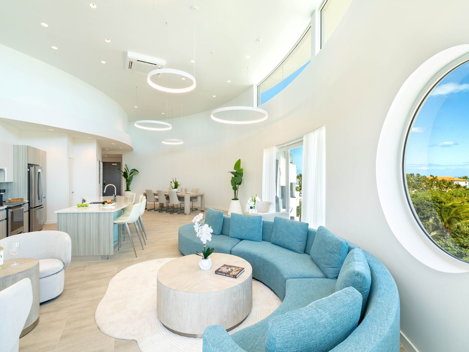 Modern open-plan living area with a circular couch and large circular window at Ellipse Grace Bay