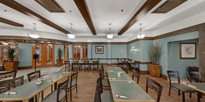 Dining room tables under pendant lights, near potted plants, in Carving Board Cafe at Glenmore Inn & Convention Centre