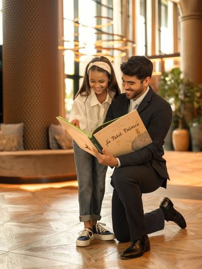 Man and girl reading a Le Petit Prince book together in hotel lobby. 