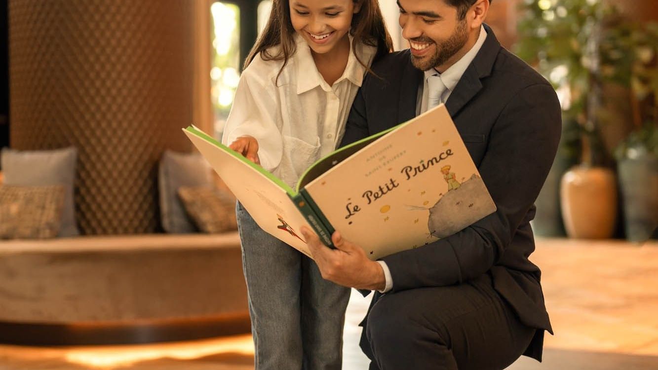 Man and girl reading a Le Petit Prince book together in hotel lobby. 