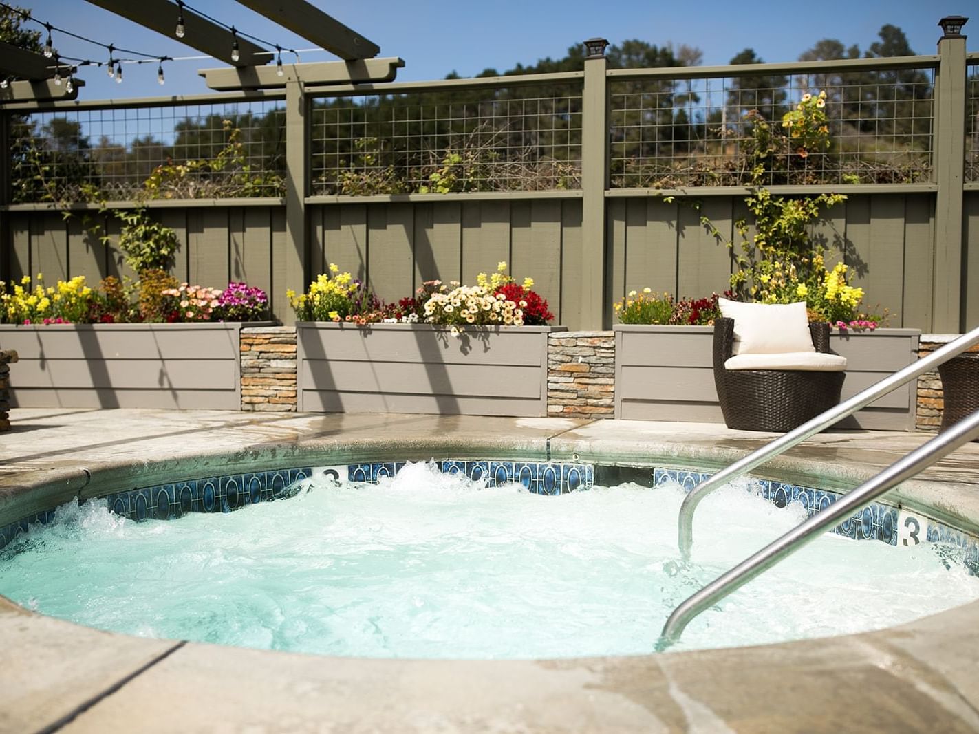 Bubbling hot tub by floral planters under a wooden pergola with a lounge chair at Sea Otter Inn, Cambria