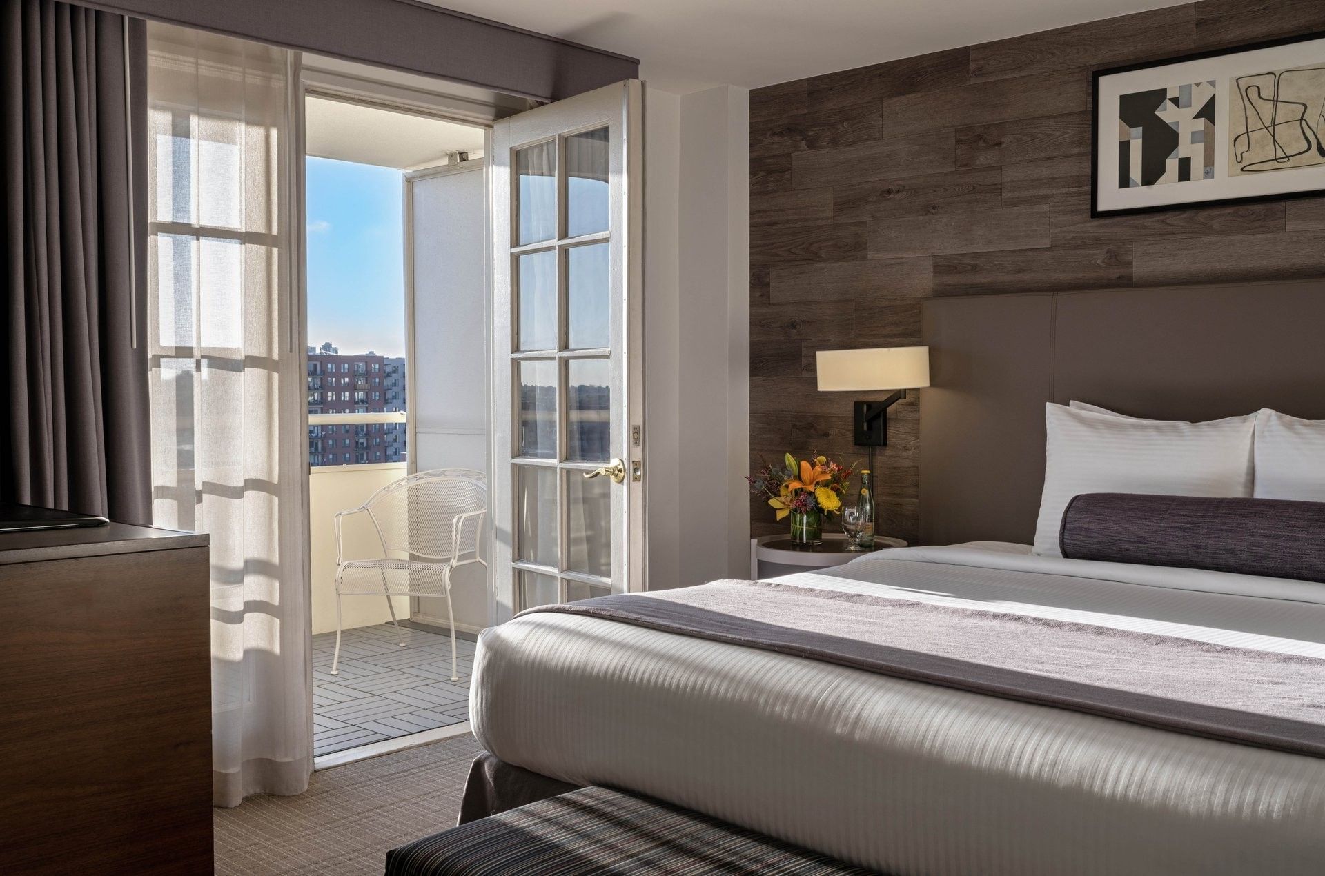 White balcony chair by a glass door in a guestroom with a wood wall in Executive Suites at Warwick Denver