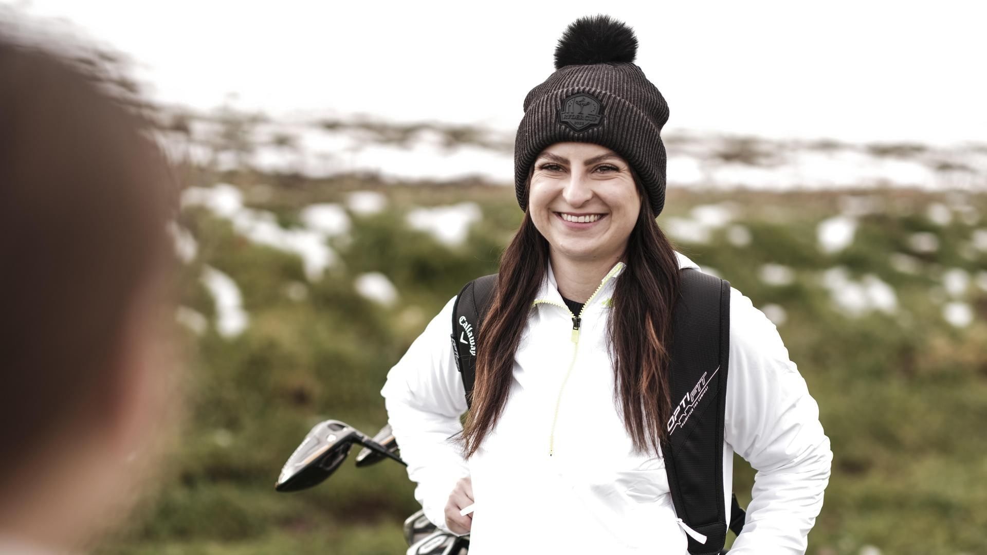 Lächelnde Frau mit Bommelmütze und Golfausrüstung auf winterlichem Golfplatz im Falkensteiner Balance Resort Stegersbach