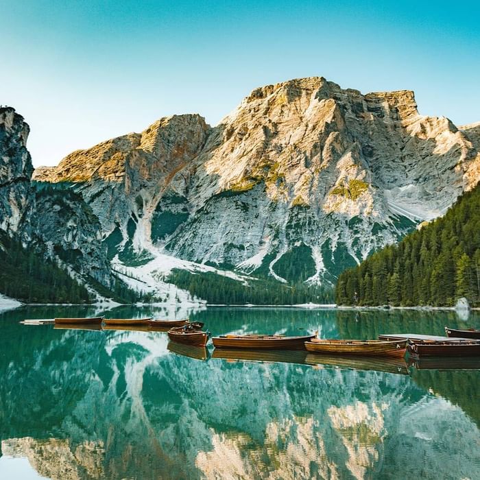 Lago calmo con canoe e riflessi di montagne innevate sotto un cielo blu.