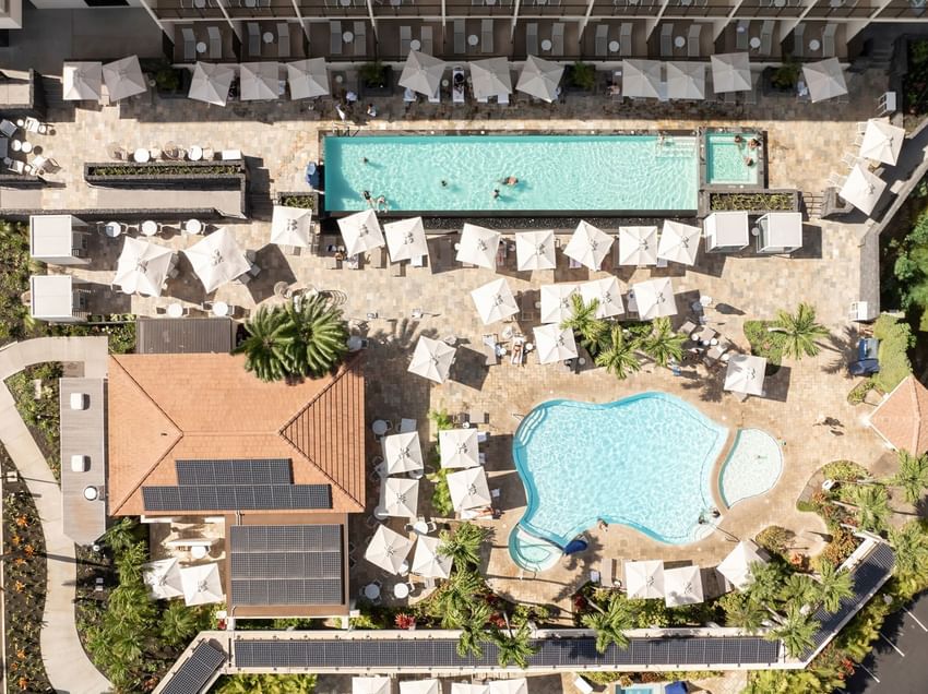 Aerial view of the hotel's pool area with a large swimming pool, lounge chairs, umbrellas, and solar panels on the roof of a building.