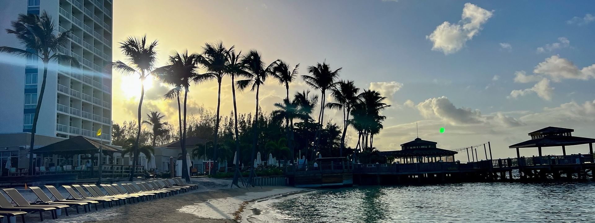 Golden sunset over a sandy beach by a row of lounge chairs and palm trees at Warwick Paradise Island Bahamas