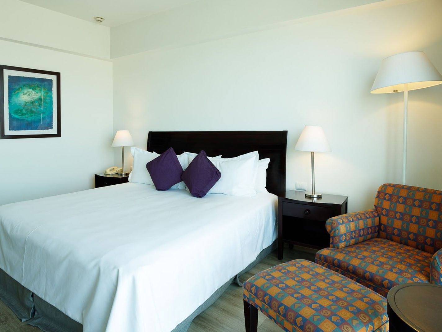 King Deluxe room with a dark wood headboard, blue wall art, and a matching patterned ottoman at Camino Real Pachuca