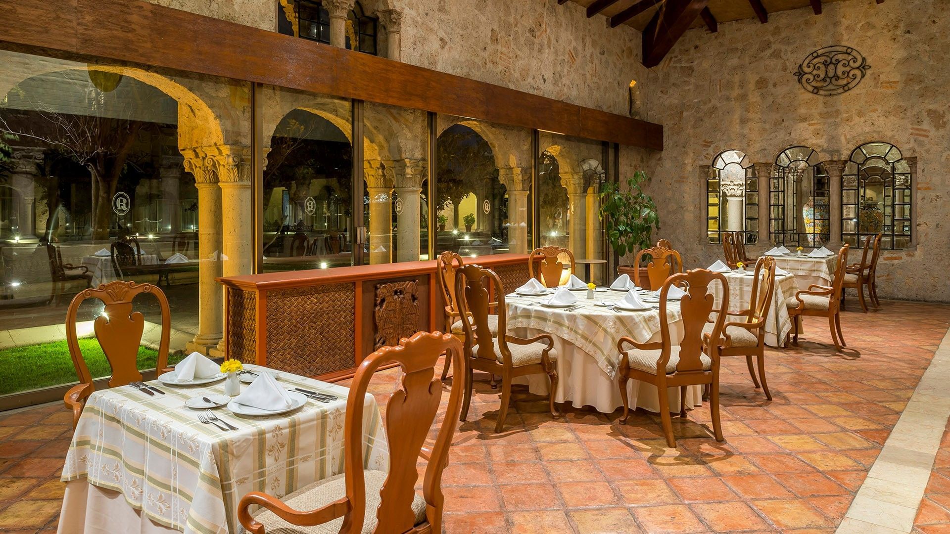 Elegant restaurant with terracotta floors, wooden chairs, white-clothed tables, and stone walls at Quinta Real Aguascalientes