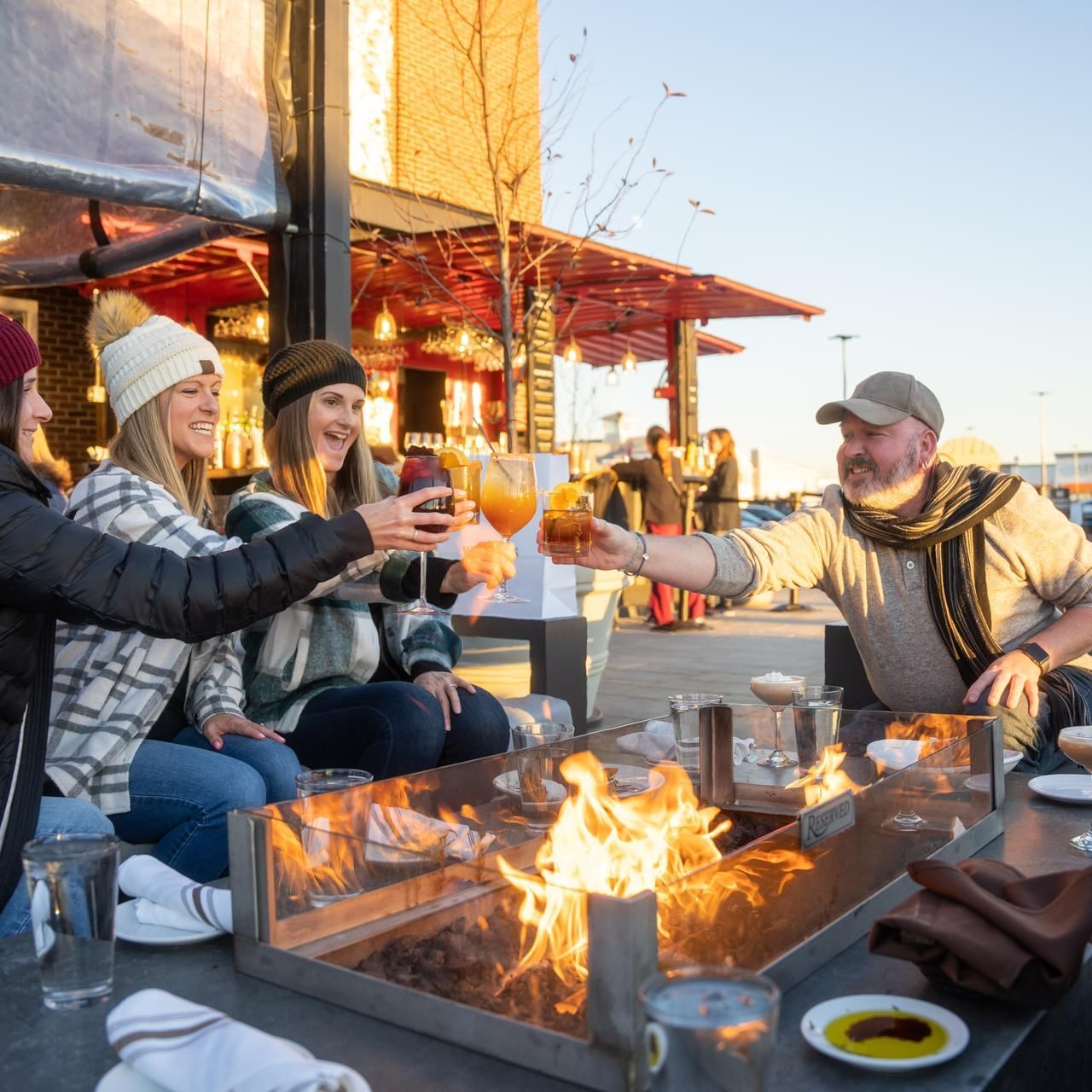 Friends toasting beer by a fireplace in Tuscan Market at The Artisan Hotel at Tuscan Village