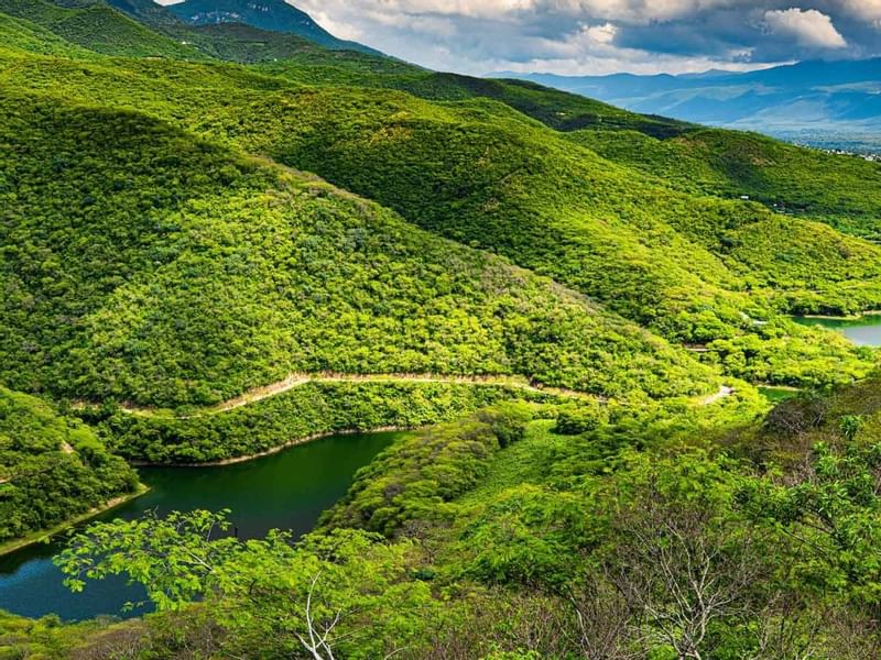 Winding river surrounded by lush green hills under a cloudy sky, creating a tranquil landscape near Grand Fiesta Americana