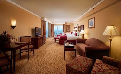 room with two beds, sofa, small table and dresser with televisio