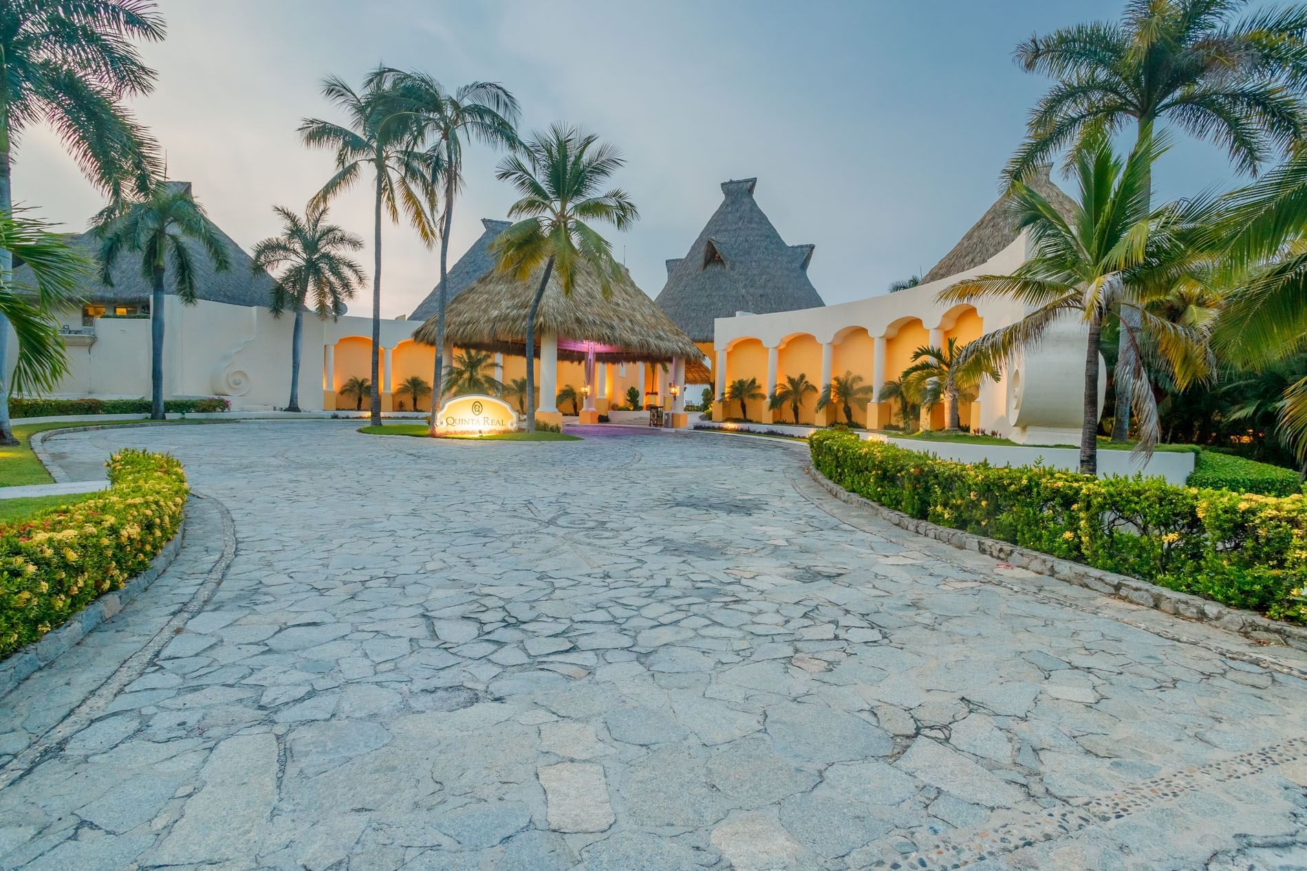 Scenic paved driveway leading to the Quinta Real Acapulco entrance sign, surrounded by lush tropical palm trees