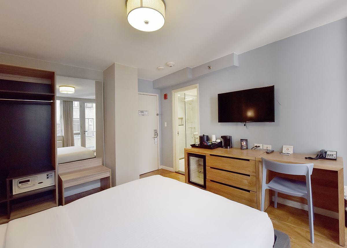 A wide-angle view of a hotel room with a queen-sized bed, desk, TV, and mini-fridge.