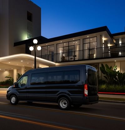 Sleek black shuttle van parked in front of a modern hotel entrance in twilight at The Harrison Hotel Downtown Hollywood