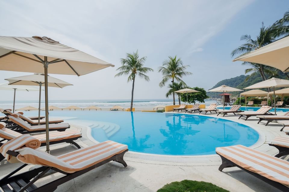 Infinity pool with striped loungers and white umbrellas overlooking the sandy beach at Quinta Real Acapulco