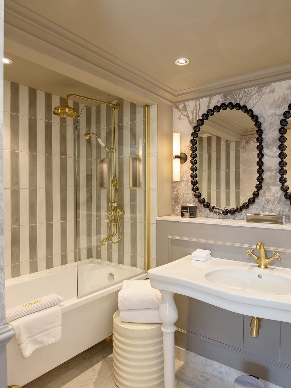 Elegant bathroom with double sinks, round mirrors, and bathtub in Penthouse at The Capital Hotel