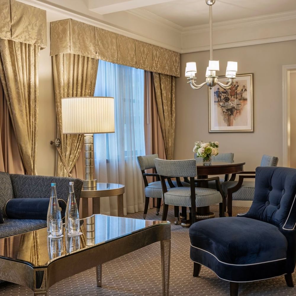 On The Avenue One Bedroom Suite lounge with a velvet blue chair with glass table, and dining corner at Warwick New York