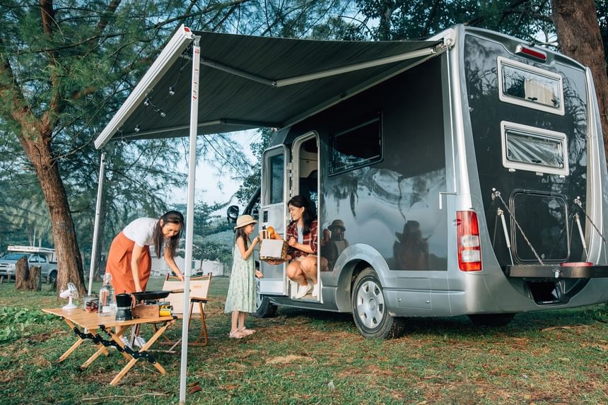 Two adults and a child cooking outdoors next to a large silver camper van at Fall Creek Marina & Campground
