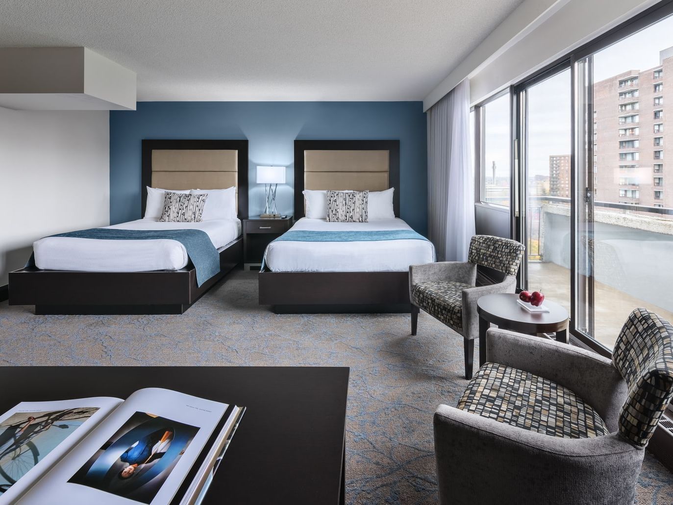 room with two beds and accent chairs near door to balcony