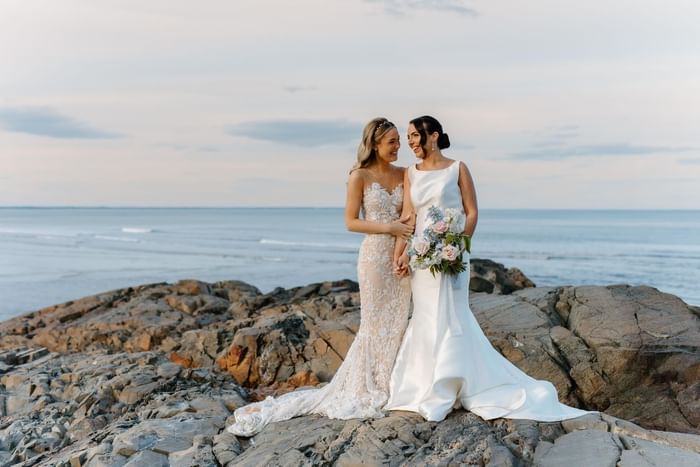 Two brides posing on a boulder by the sea at Ogunquit Collection