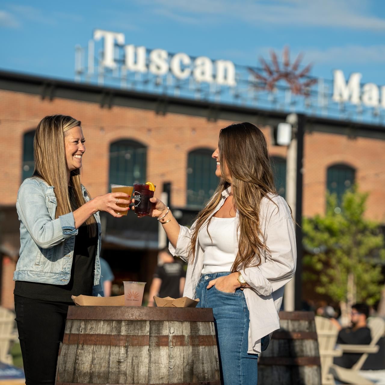 Two ladies toasting beer over a barrel near Tuscan Market at The Artisan Hotel at Tuscan Village