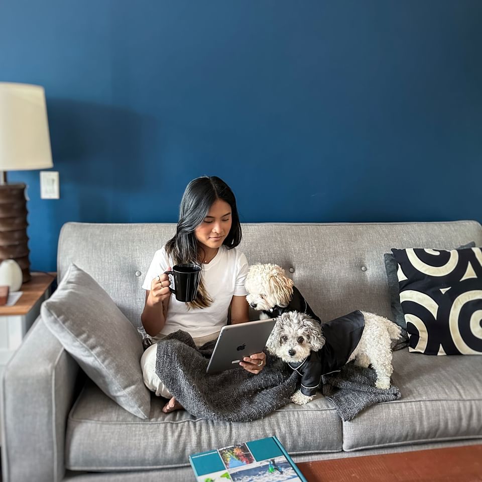 A young lady on a hotel room couch snuggling with her small dog