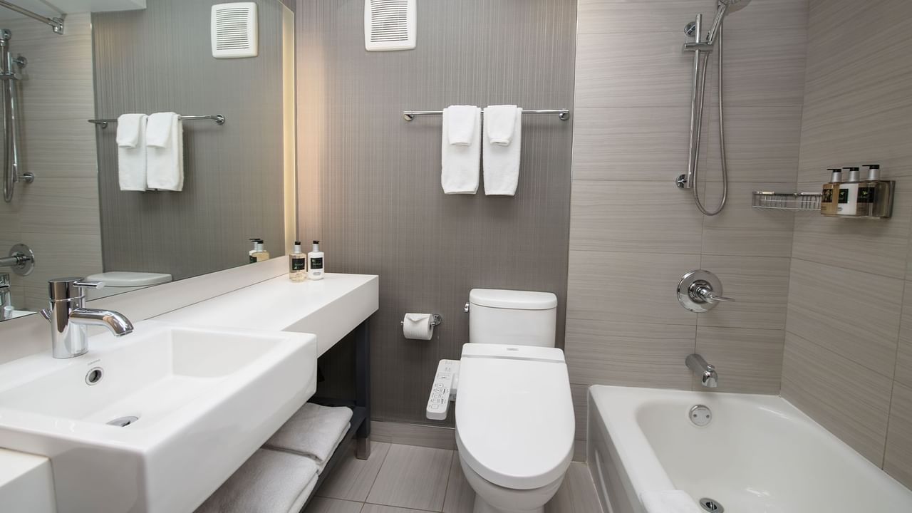 Sink, toilet, and bathtub in a hotel bathroom with a mirror and towels.