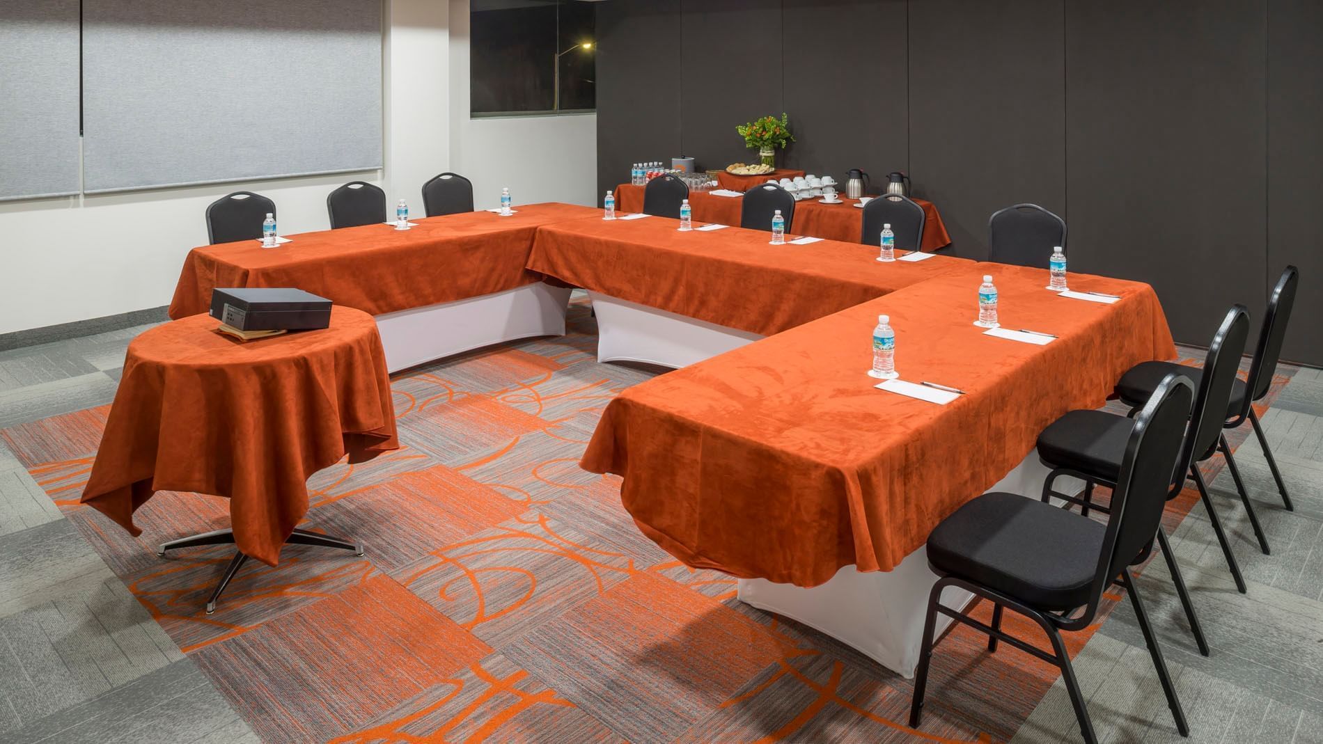 Kyoto meeting room with a U-shaped table, orange linens, bottled water, and black seating at Real Inn Celaya