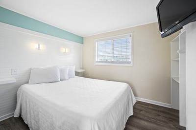 Deluxe Queen Suite bedroom with a queen bed, light wood flooring, and a window with blinds at Madison Beach Motel