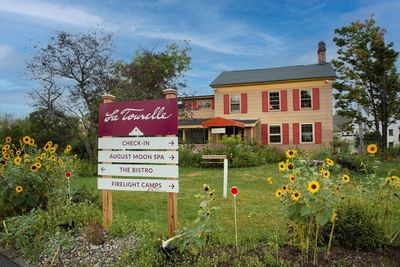 Directional sign pointing to August Moon Spa, Bistro, and Check-in near sunflowers at La Tourelle Hotel and Spa