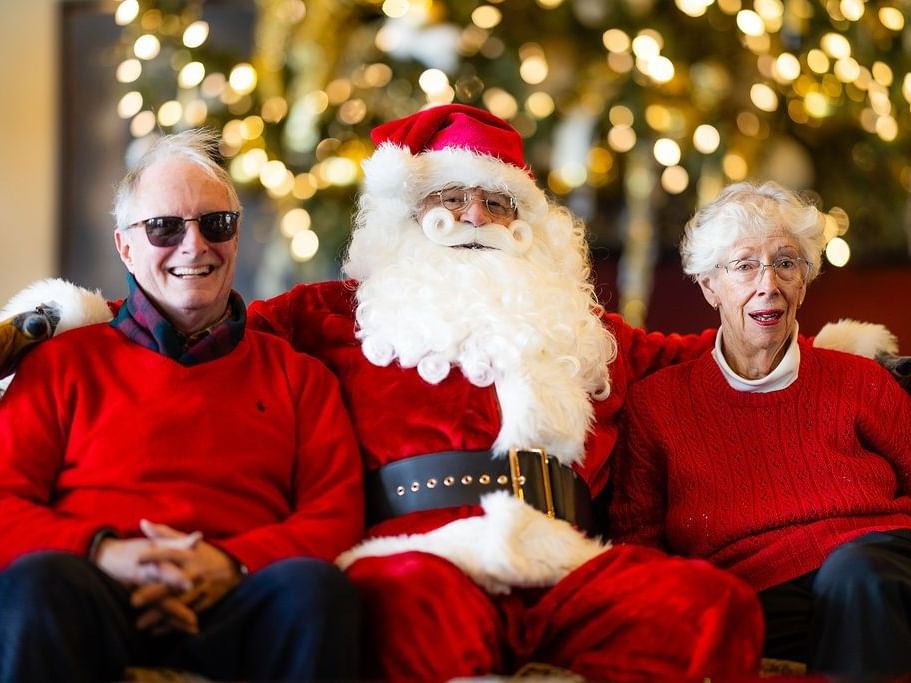 Santa Claus sitting between a smiling elderly couple in red sweaters at Spring Creek Resorts, featuring Canmore events