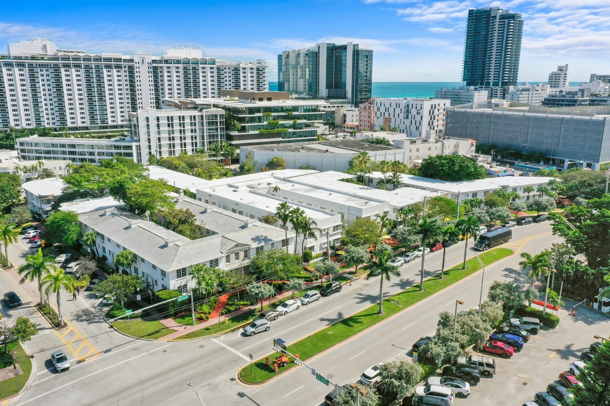An aerial view of a white hotel building with palm trees and a parking lot.