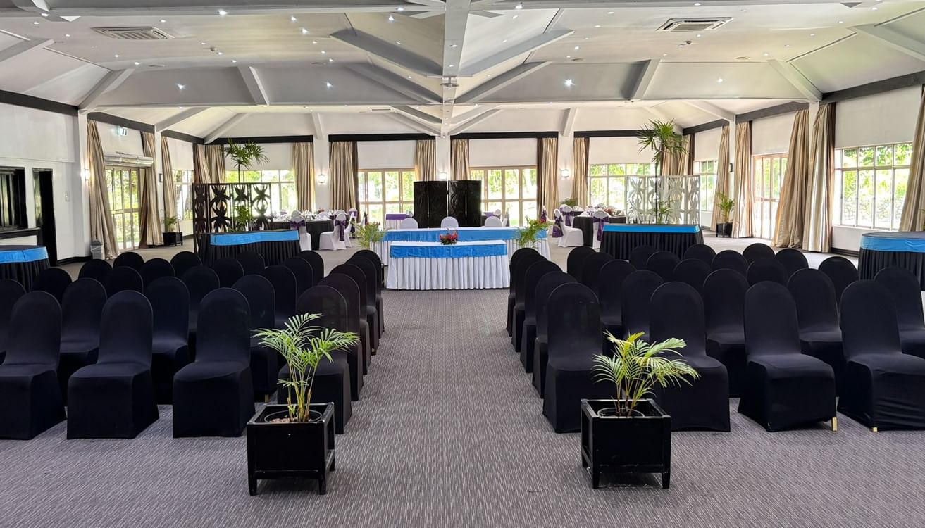 Large indoor event space with rows of black chairs, carpeted floor, and potted plants at Warwick Fiji Resort and Spa