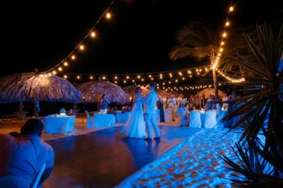 Couple dancing under string lights at a romantic beach wedding reception at Amsterdam Manor Beach Resort