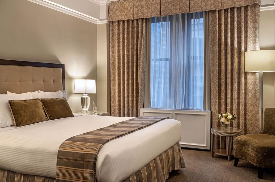 Elegant hotel room with large bed, chair, and window at Warwick New York