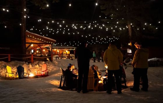 People gather around a fire pit under string lights at night at Aava Whistler