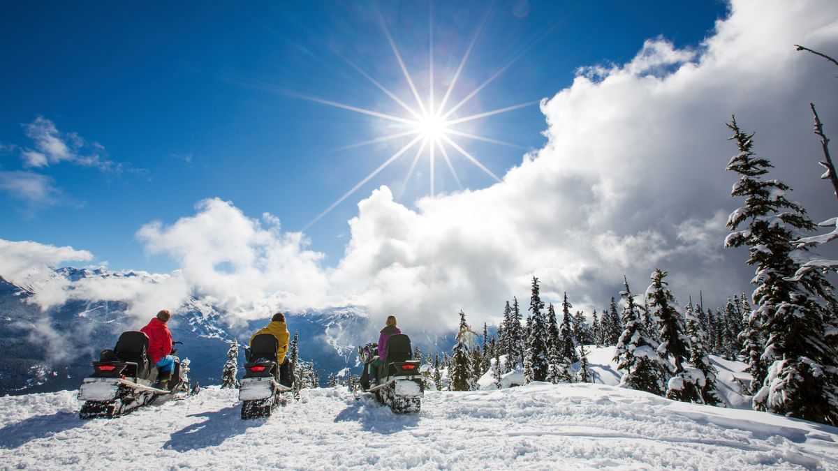 People riding snowmobiles on a snowy trail near Blackcomb Springs Suites