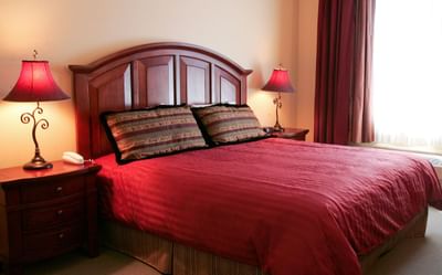 A king-sized bed with a dark wood headboard and two nightstands with red lamps at The Pointe at Castle Hill