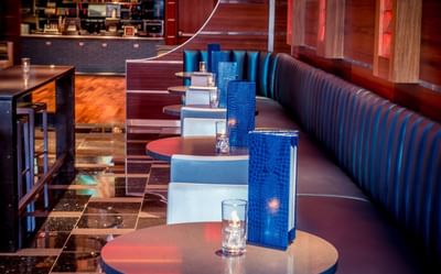 Round tables with menus & candles lined up beside a long tufted booth in Harborside Bar and Lounge at Harborside Inn Boston