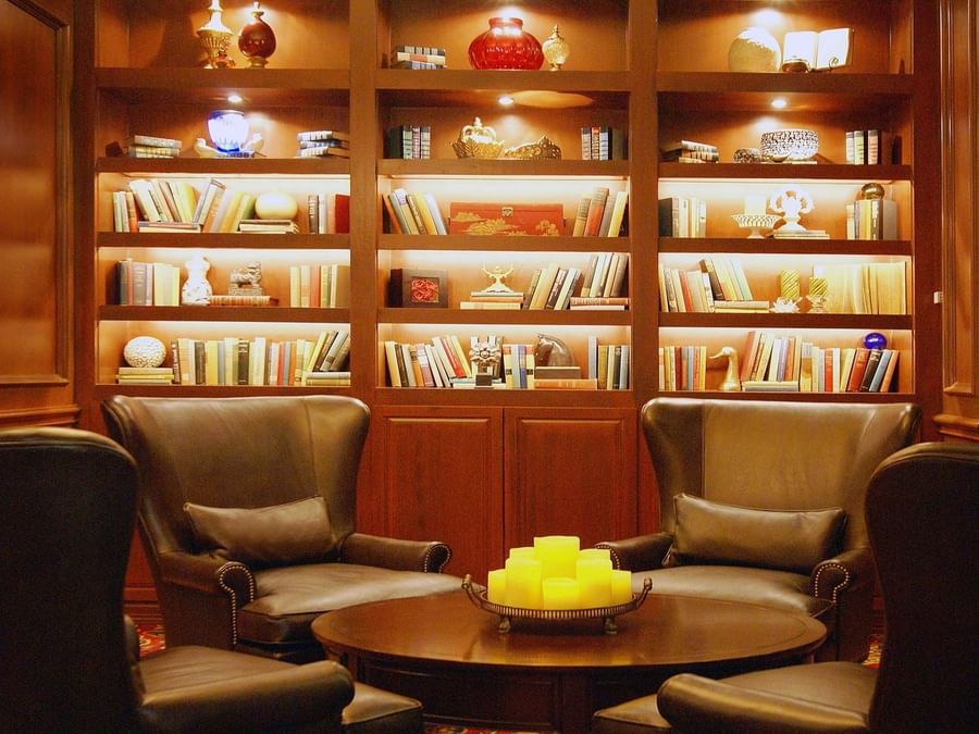 Cozy lounge area with leather wingback chairs, built-in bookshelves, and a candle-topped round table at The Library Bar