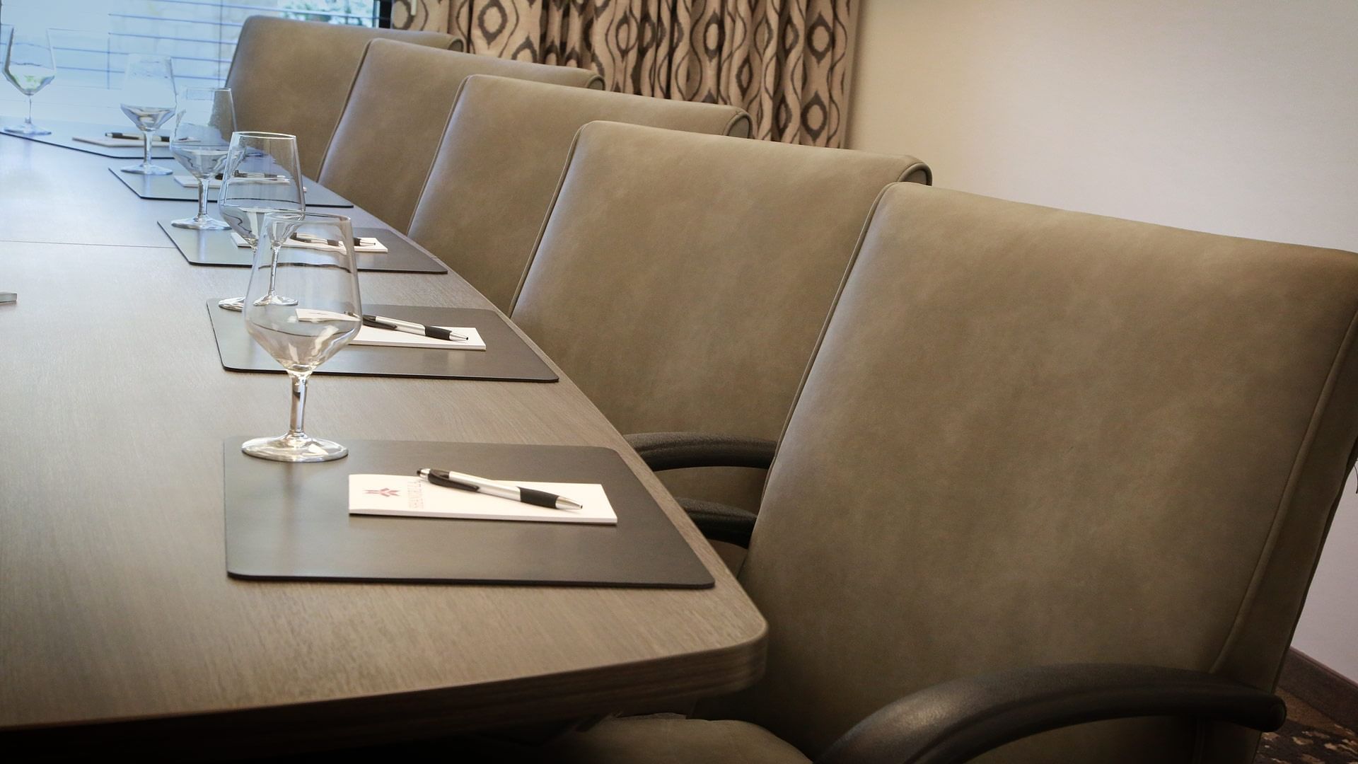 Modern conference table set with water glasses, pens, and notepads in Boardroom at  Shangri-La Monkey Island