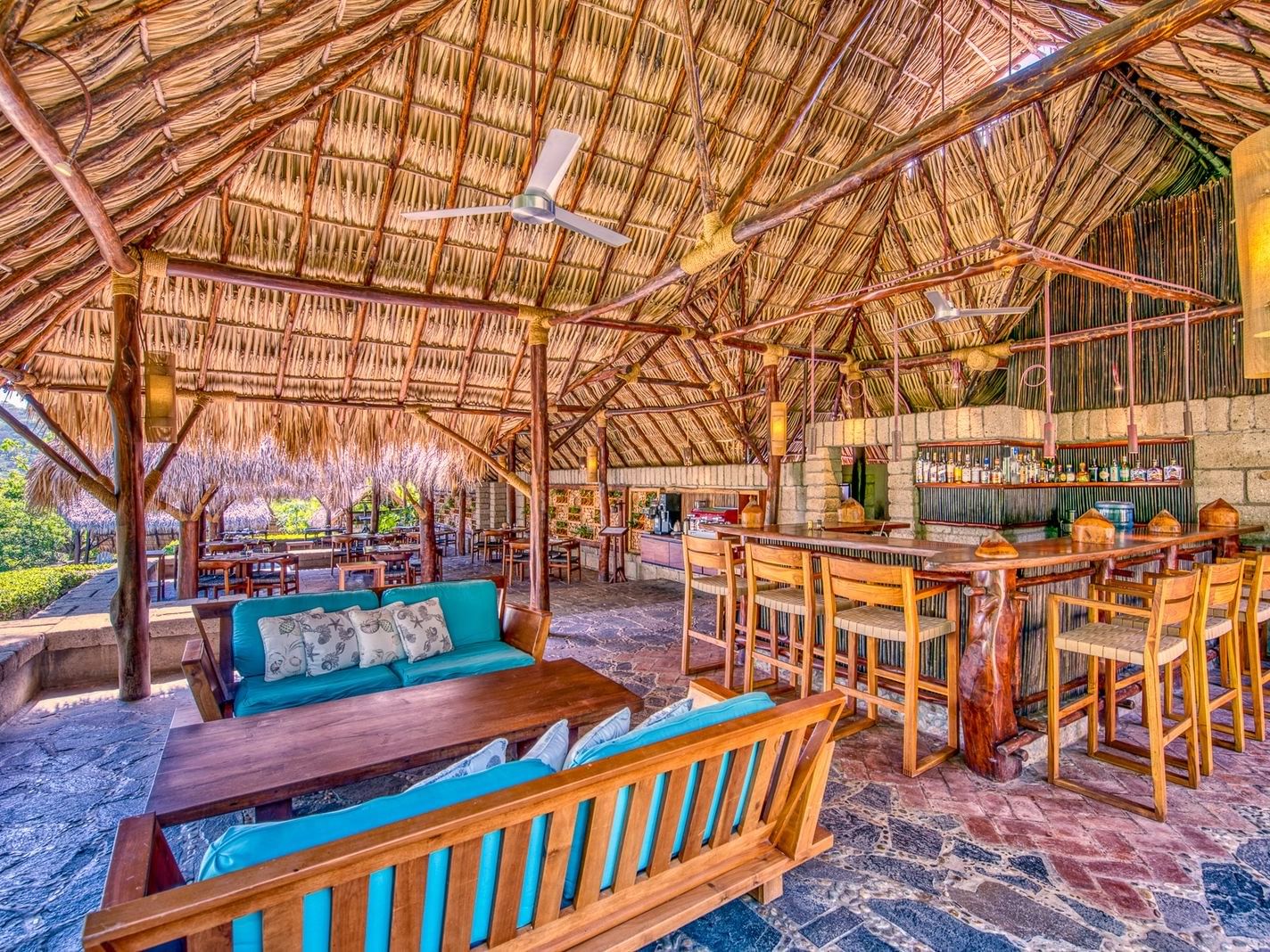 Blue sofas by a wood bar under a high thatched roof in Commodore Bar at Morgan's Rock Reserve & Ecolodge