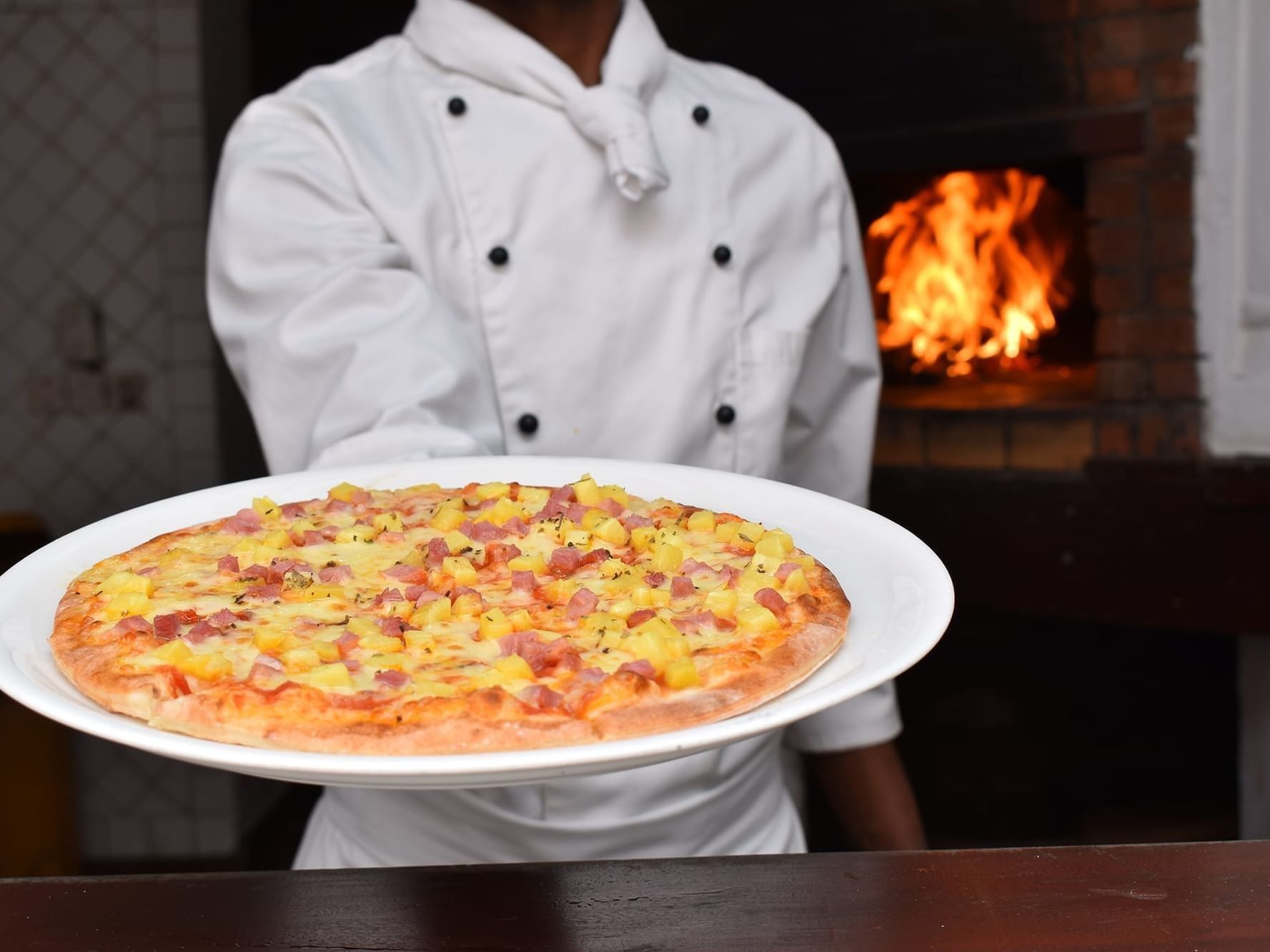 Chef holding a plate with pineapple ham pizza in front of a fire oven at Serena Beach Resort & Spa Mombasa.