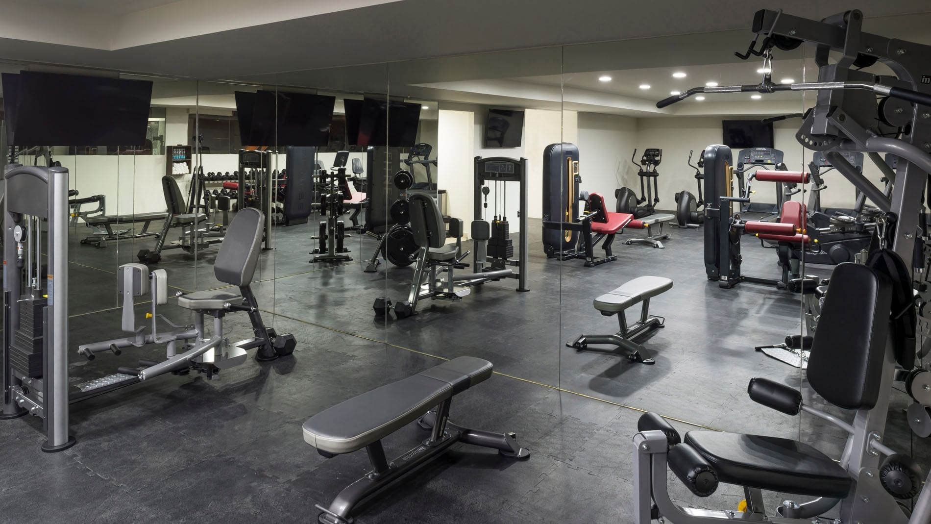 Modern gym at Real Inn Celaya featuring wall-to-wall mirrors, strength training equipment, and flat screens