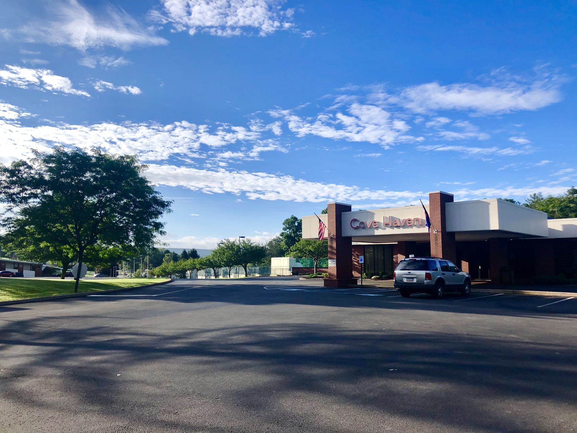 Exterior view of Cove Haven with a cloudy blue sky, green trees, and a parked gray SUV in the foreground