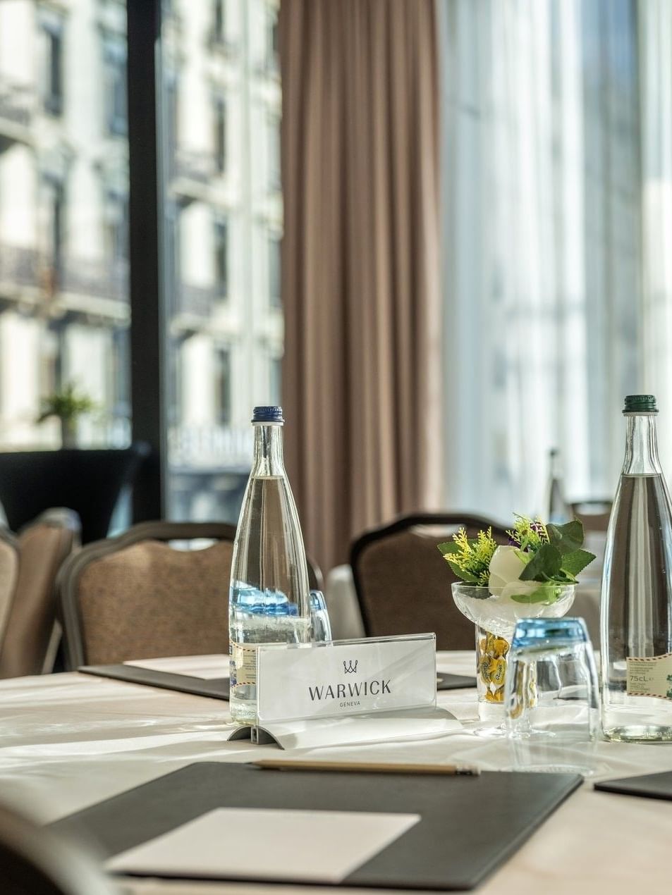 Water bottles by note pads and blue glasses on a linen table in Rigi + Cervin at Warwick Geneva