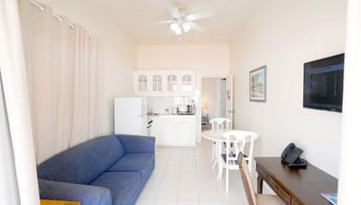 Blue sofa and white dining set beside a dark wood desk with a small kitchen in Junior One Bedroom at Worthing Court Apartment
