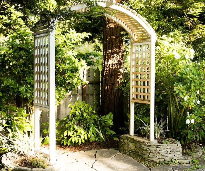 White wooden archway with lattice panels in lush garden with stone path and flowering plants.