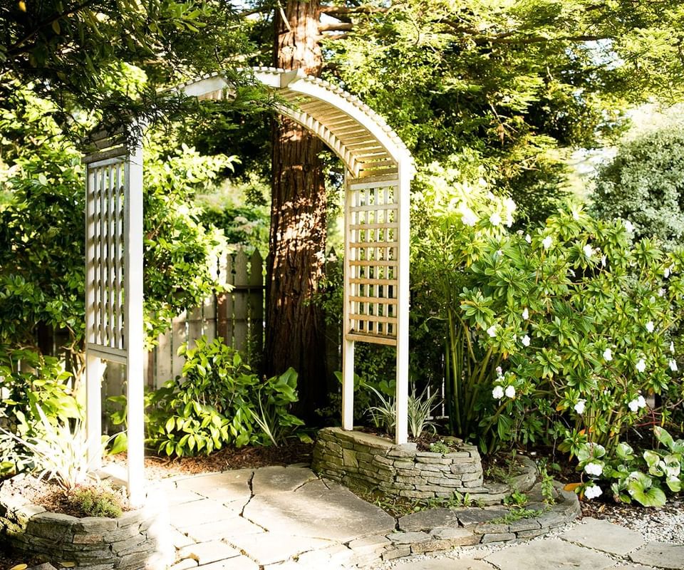 White wooden archway with lattice panels in lush garden with stone path and flowering plants.